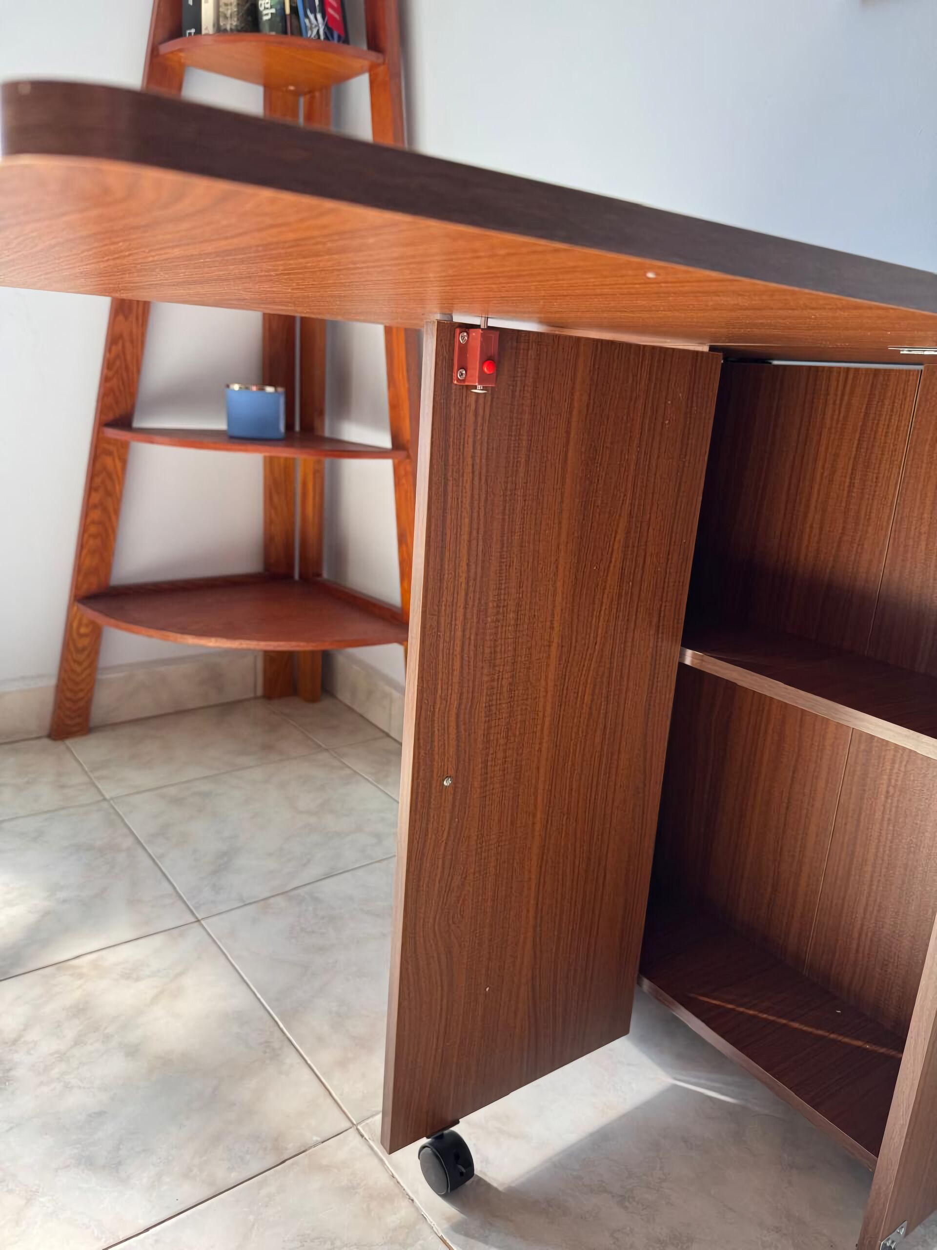 A wooden desk with a shelf and a drawer, a small blue container, and a black object on the floor.