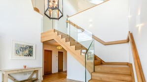 Un escalier moderne avec des rampes en verre et des marches en bois, menant à l’étage supérieur.