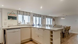 A modern kitchen with a dishwasher, a sink, and a dining area with chairs. - 3 Bed in Aldeburgh (oc-o5630) (Aldeburgh)