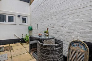 A small outdoor patio with wicker furniture, a table, and a bottle of wine. - 3 Bed in Aldeburgh (oc-o5630) (Aldeburgh)