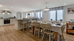 A modern kitchen with a dining area, wooden flooring, and large windows. - 3 Bed in Aldeburgh (oc-o5630) (Aldeburgh)