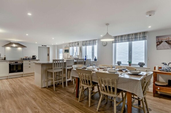 A modern kitchen with a dining area, wooden flooring, and large windows. - 3 Bed in Aldeburgh (oc-o5630) (Aldeburgh)