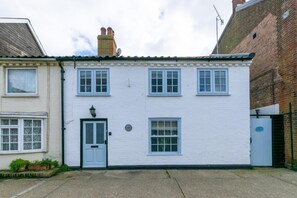 A two-story white building with a grey door, multiple windows, and a small garden area with plants. - 3 Bed in Aldeburgh (oc-o5630) (Aldeburgh)