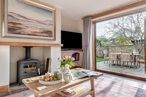 Ein gemütliches Wohnzimmer mit Kamin, einer Essecke mit Tisch und Stühlen, einem Fernseher und einem großen Fenster mit Blick auf einen Garten.