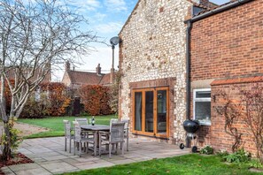 Ein Haus aus Stein und Ziegel mit Terrasse, Sitzgelegenheit und Grill.