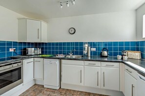 A kitchen with white cabinets, a blue tiled backsplash, a stainless steel kettle, and a clock on the wall. - 3 Bed in Blue Anchor (oc-b28903) (Blue Anchor)