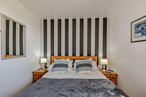 A bedroom with a striped wall, a wooden bed frame, two bedside tables with lamps, and a framed picture on the wall. - 3 Bed in Blue Anchor (oc-b28903) (Blue Anchor)