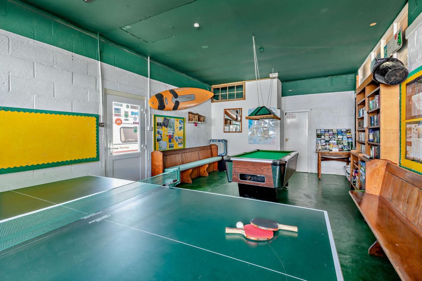 A room with a pool table, a billiards table, and a bookshelf.