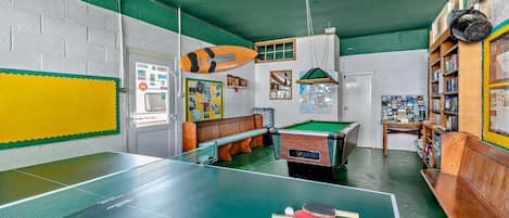 Una habitación con mesa de billar, estantería y mesa de futbolín.