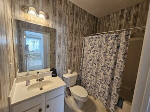 Een badkamer met een houten wand, een wit wastafelmeubel, een toilet en een douchegordijn met een motief van vlinders.