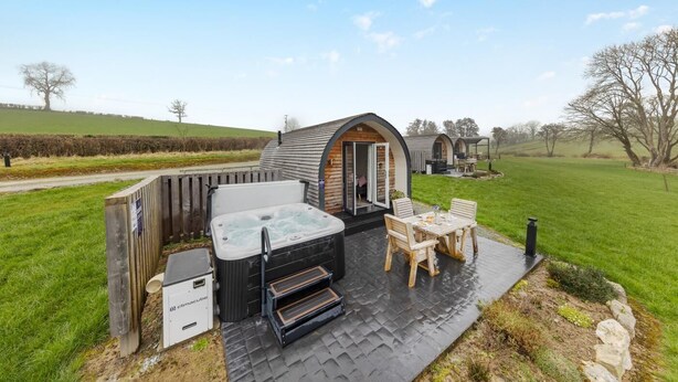 Ein gemütlicher Bereich mit Whirlpool im Freien, einer Holzterrasse, einem Tisch mit Stühlen und einem kleinen Holzhaus mit offener Tür.