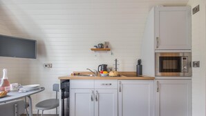 Eine kleine Küche mit einer Holzausstattung, einem Spülbecken, einer Mikrowelle und einem kleinen Regal darüber.