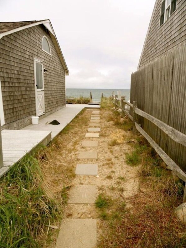 A pathway leading to beach houses with a wooden fence on one side and a grassy area on the other.