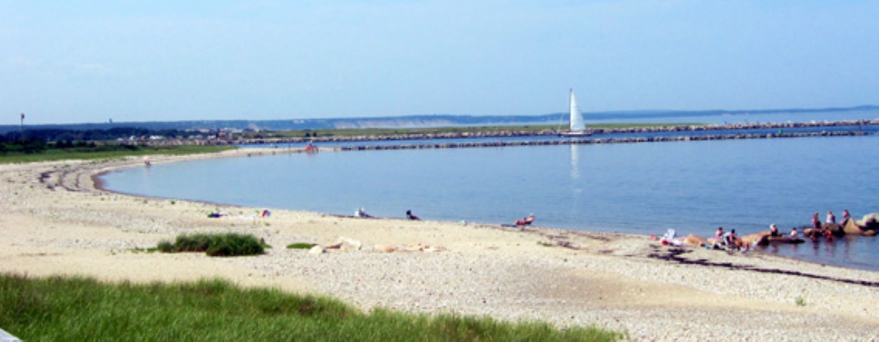 Een strand met mensen die zonnebaden en een zeilboot in de verte.