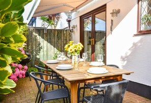 An outdoor wooden table set for dining with chairs, a grill, and a flower vase.