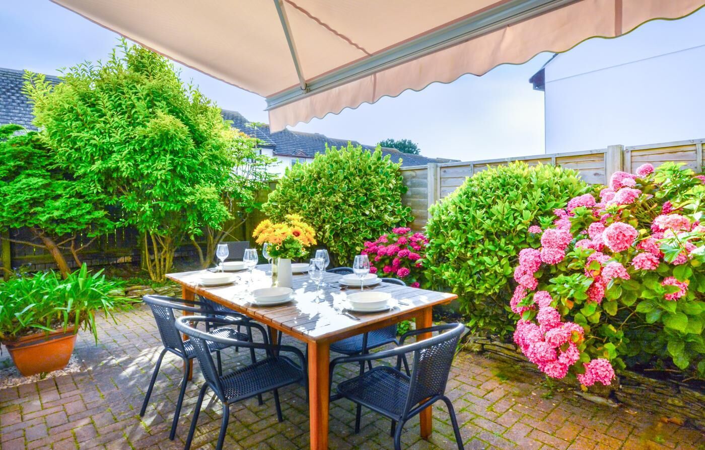 An outdoor patio with a table set for dining, surrounded by lush greenery and flowering plants.