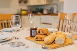 A dining table with plates, cutlery, wine glasses, and a wooden board with pastries and a jar of jam.