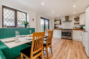 A modern kitchen with a dining area, featuring a green bench, wooden chairs, and a large window with a view.