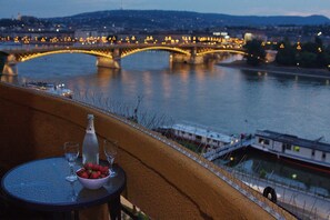 A table with a bottle, glasses, and a bowl of strawberries, overlooking a river with a bridge and city lights. - Riverside Gem in the center of Budapest is two-bedroom, cozy and comfortable (Budapest)
