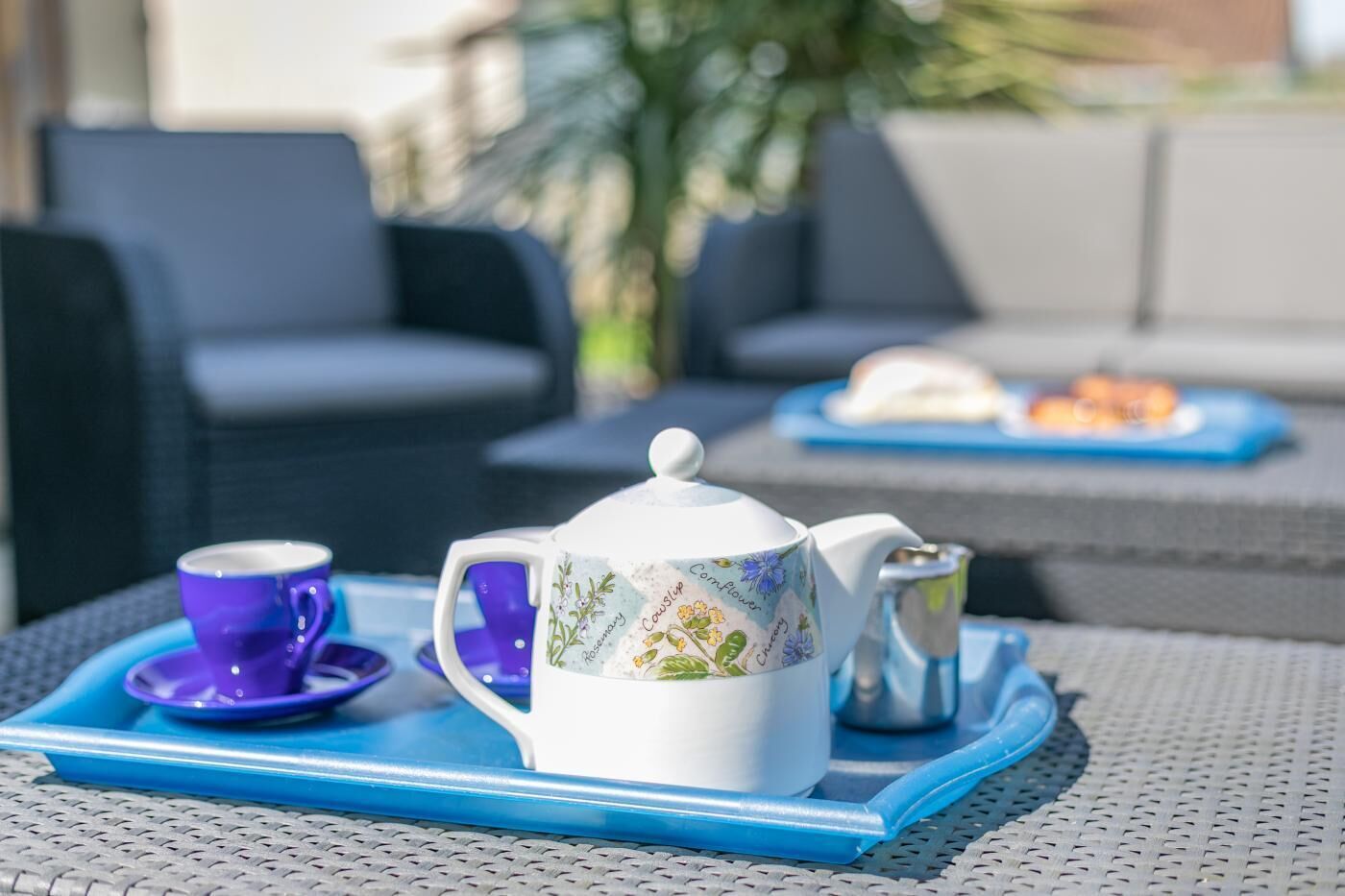 Uma mesa posta com um bule, xícara e açucareiro sobre uma bandeja azul.