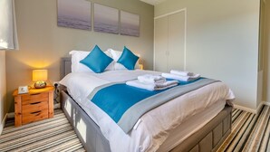 Quarto de hotel com uma cama, mesa de cabeceira com abajur, obra de arte na parede e guarda-roupa.