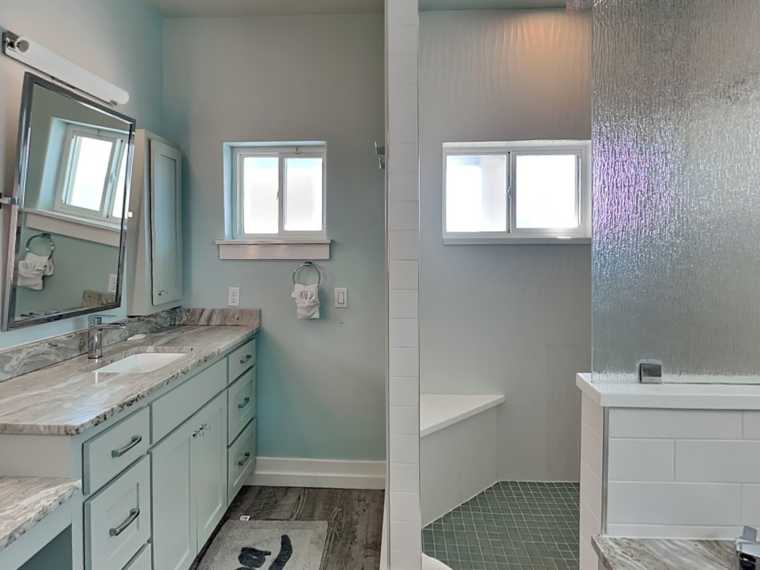 A bathroom with a marble countertop, a sink, a mirror, a towel rack, and a shower area with a glass door.