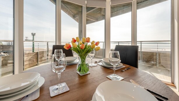 A dining table with tulips, wine glasses, and plates, overlooking a coastal view. - 2 Bed in Tenby (oc-t29060) (Tenby)