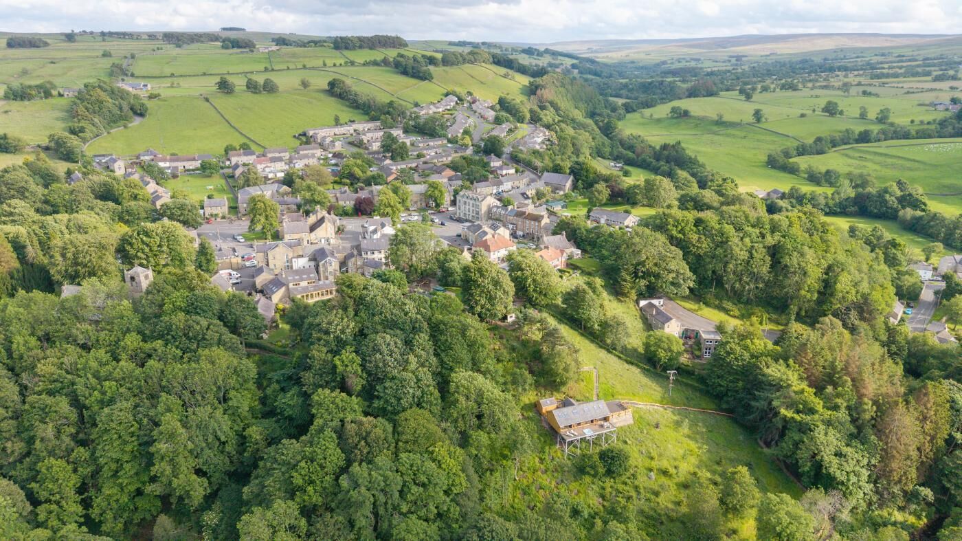 Vista aérea de uma aldeia com casas rodeadas por vegetação exuberante e colinas ondulantes.