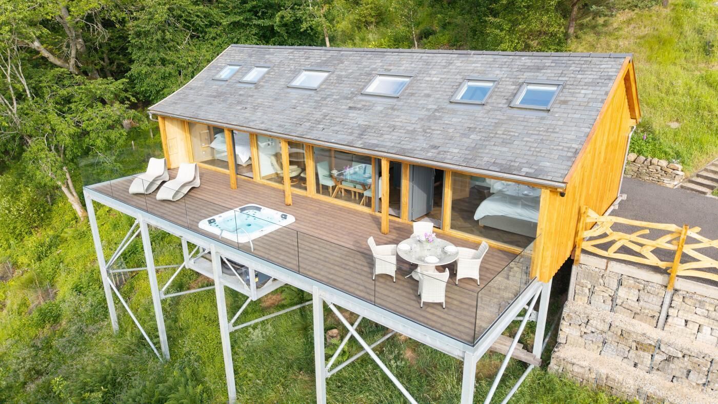 Eine Holzterrasse mit Whirlpool, Sitzgelegenheit im Freien und einem Schlafzimmer mit Fenster.