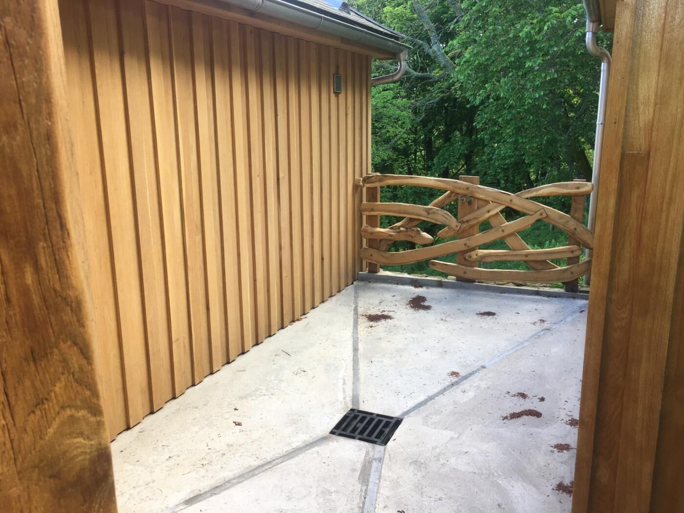 A wooden building with a metal gate, a concrete floor, and a drainpipe.