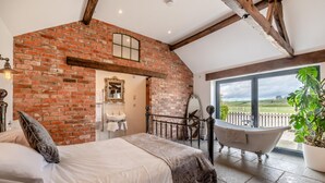 Une chambre avec un mur en briques, un lit, une salle de bain avec une baignoire et une vue sur la campagne.