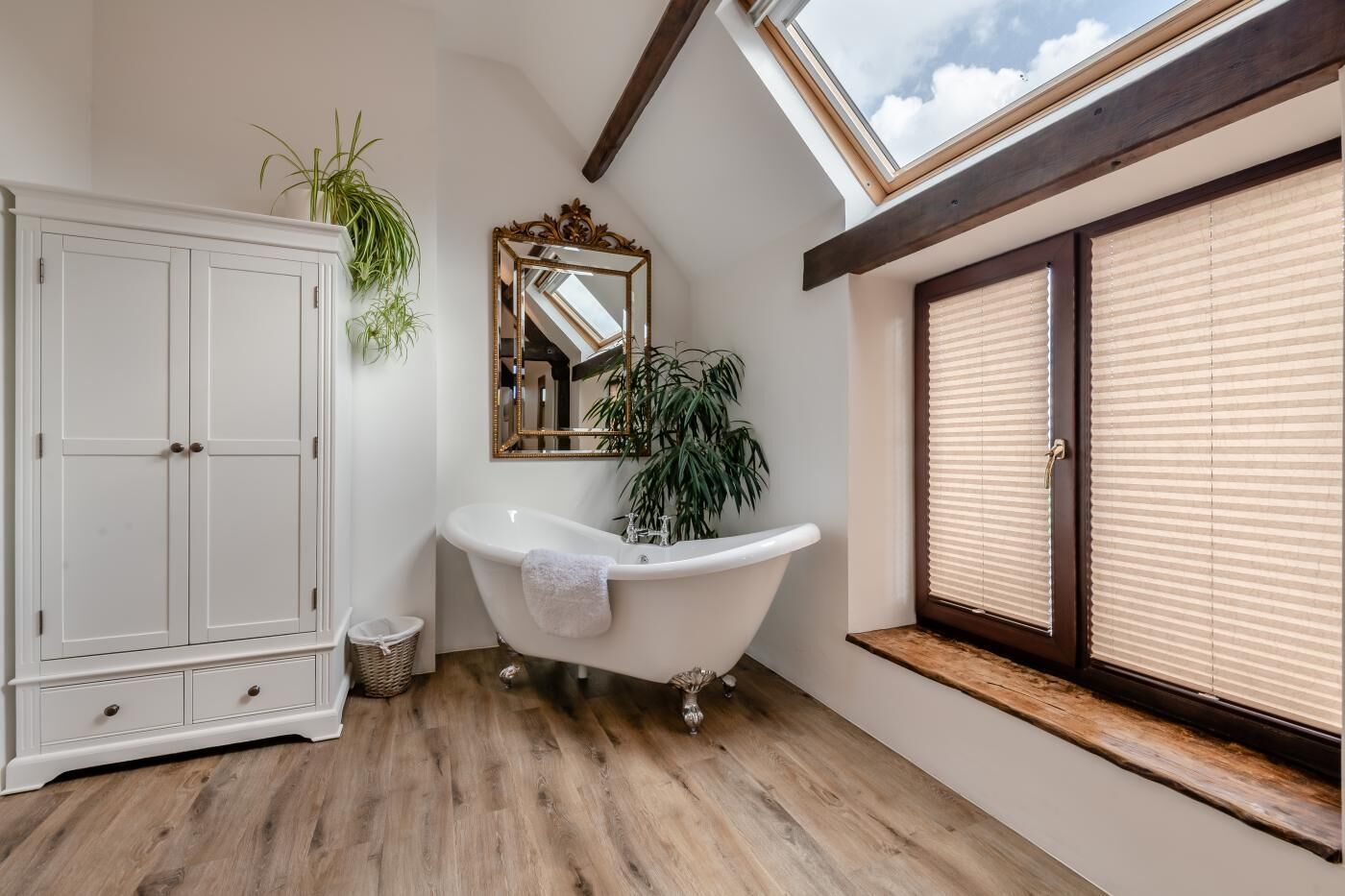 A bathroom with a clawfoot bathtub, a white wardrobe, a mirror, and a window with blinds.