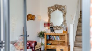 Una sala de estar acogedora con un espejo grande y ornamentado, una estantería, un sillón de cuero y una escalera que sube a otro nivel.