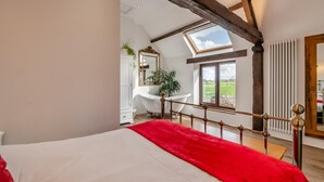 Un dormitorio con una cama grande, un plaid rojo, un tragaluz, un armario blanco y una bañera blanca, con vistas al exterior.