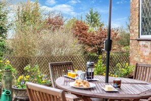 An outdoor dining area with a table set for breakfast, including croissants, a coffee pot, and a glass of orange juice.