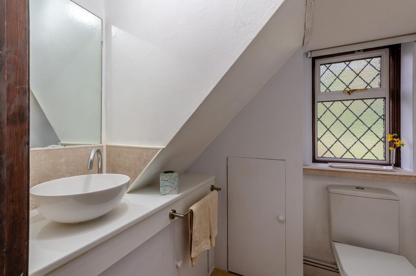 Un baño con lavamanos blanco, un espejo, inodoro y ventana con diseño de celosía.