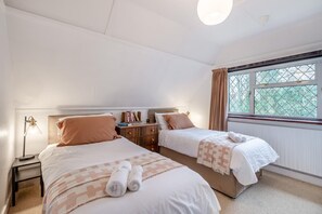 A bedroom with two beds, a nightstand, a lamp, and a window with curtains.