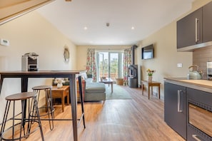 A modern kitchen with a central island, bar stools, a dining area with a sofa, and a large window with curtains. - 1 Bed in Pershore (oc-t29051) (Pershore)