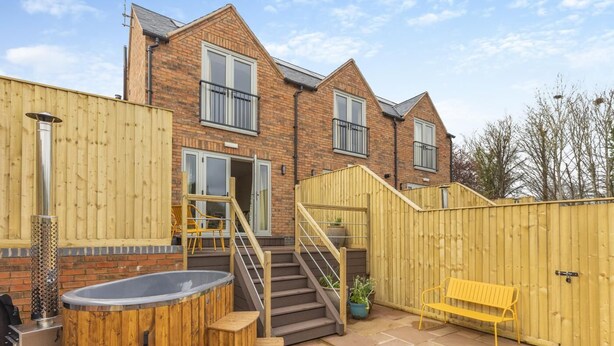 A two-story brick house with a wooden fence, a hot tub, and a bench.