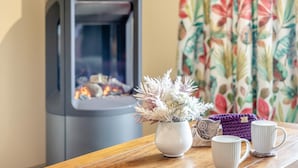 Una habitació acollidora amb una llar de foc, una taula de fusta i un ram d'elles de flors, i un objecte de llana morada.