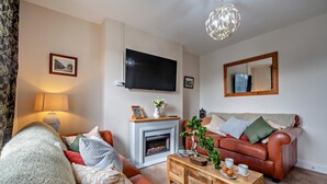 Een woonkamer met een open haard, een televisie, een bank, een salontafel en een spiegel.