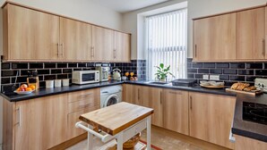 Een moderne keuken met houten kastjes, een zwart aanrecht, een wasmachine en een raam met jaloezieën.