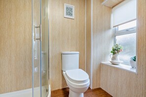Une salle de bain comprenant des toilettes, une douche en verre, une fenêtre avec vue et une petite étagère sur laquelle est posée une plante en pot.