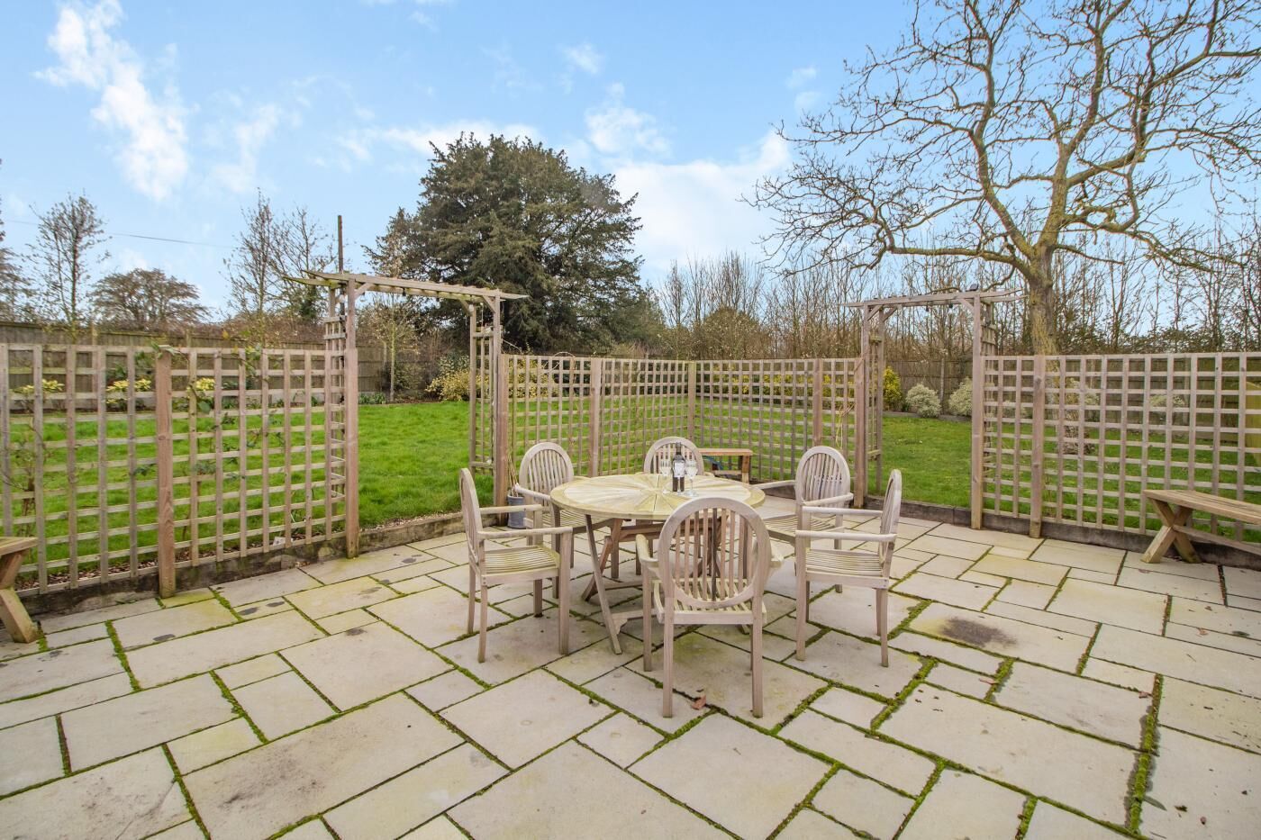 Une terrasse avec une table ronde et des chaises, entourée d’une clôture en bois.