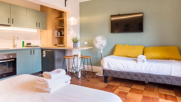 A compact room with a kitchenette, a bed with yellow pillows, a TV, and a fan. - Your Urban Escape on Emilio Vaisse Studio (Providencia)