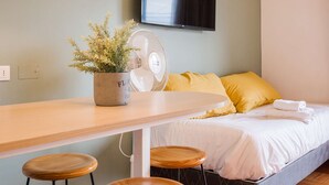 A room with a bed, a desk, a potted plant, a fan, and a television. - Your Urban Escape on Emilio Vaisse Studio (Providencia)