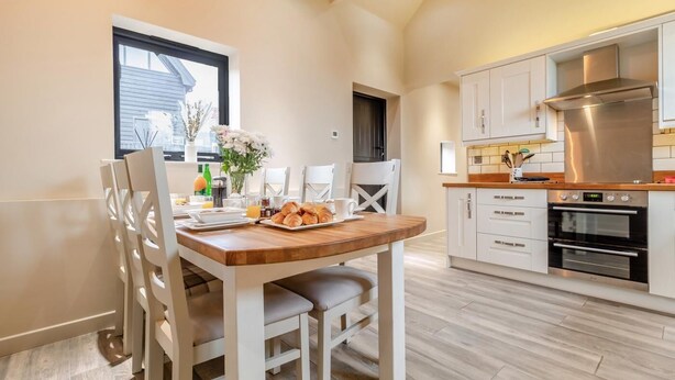 Une cuisine moderne avec des armoires blanches, une hotte de cuisinière en acier inoxydable et une table à manger en bois, accompagnée de chaises.