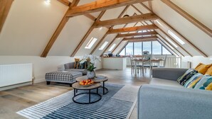Ein geräumiges Loft mit hohen Decken, freiliegenden Holzbalken, einem Essbereich und Blick durch große Fenster.