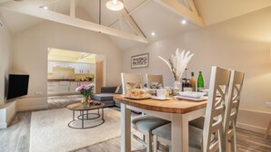 A modern living room with a dining area, a kitchen in the background, and a TV mounted on the wall. - 2 Bed in Heveningham (oc-w29029) (Heveningham)