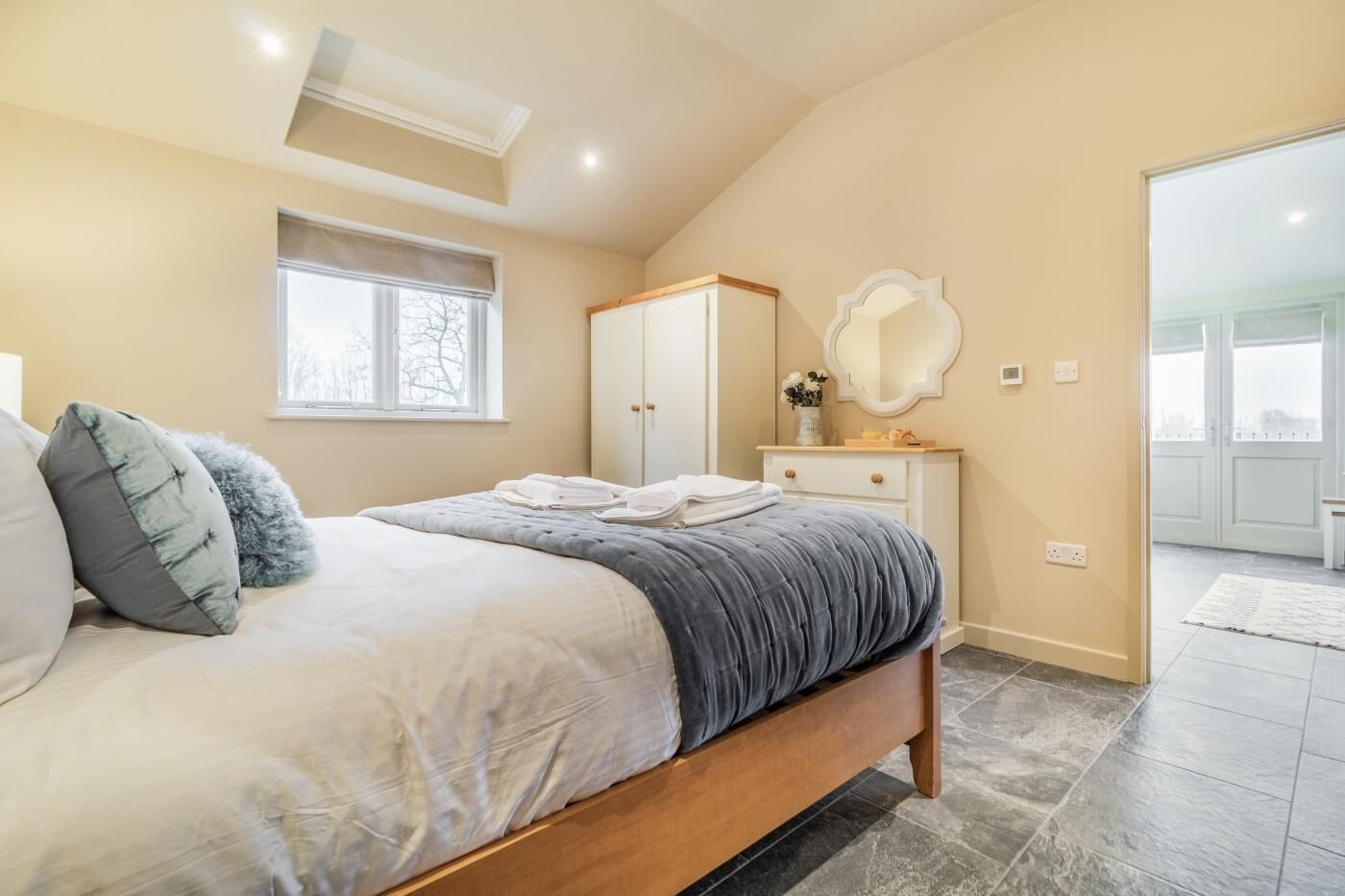 A bedroom with a bed, a dresser, a mirror, and a window.